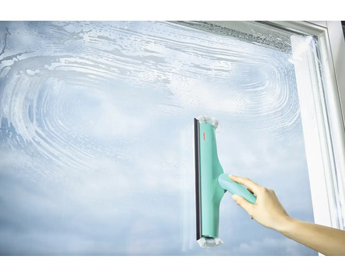 Mână curăță o suprafață de sticlă cu un racletă pentru ferestre