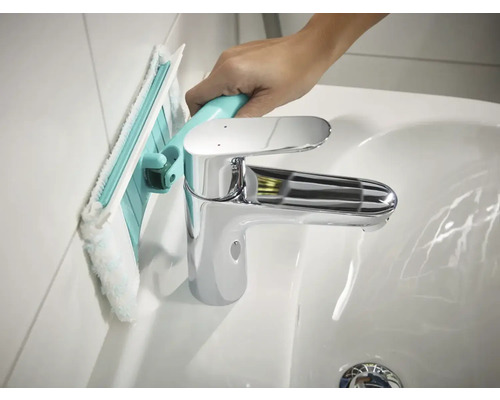 Curățarea unui perete de baie cu un raclet de baie lângă o chiuvetă.