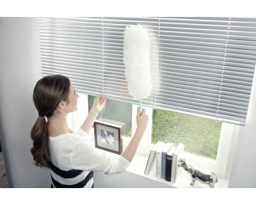 Femeie curăță jaluzele cu un pămătuf de praf