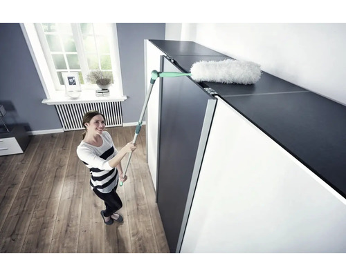 Femeie curăță suprafața unui dulap cu un mop de praf.