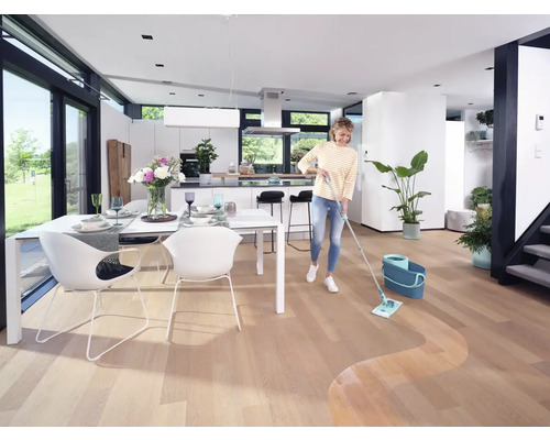 Femeie ștergând podeaua de lemn într-o sufragerie luminoasă cu mop și găleată