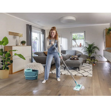 Femeie șterge podeaua de lemn cu un mop și o găleată într-un living