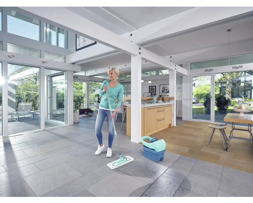 Femeie ștergând podeaua într-un living luminos cu mopul și găleata