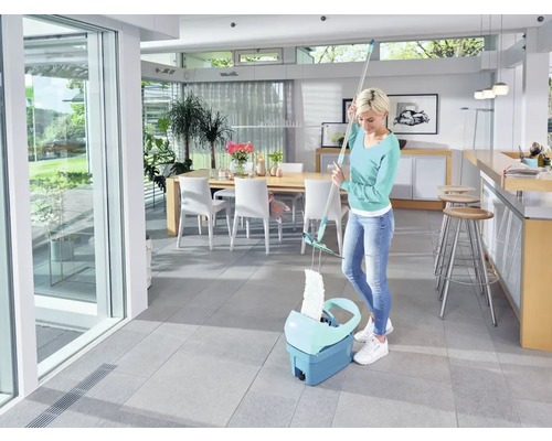 Femeie șterge podeaua cu un mop și o găleată într-o cameră luminoasă.