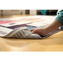 Imagine detaliată a unui covor cu model, cu o persoană care ridică colțul pentru a arăta partea inferioară