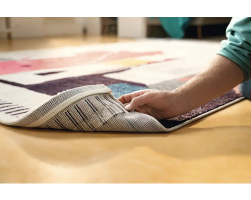 Imagine detaliată a unui covor cu model, cu o persoană care ridică colțul pentru a arăta partea inferioară