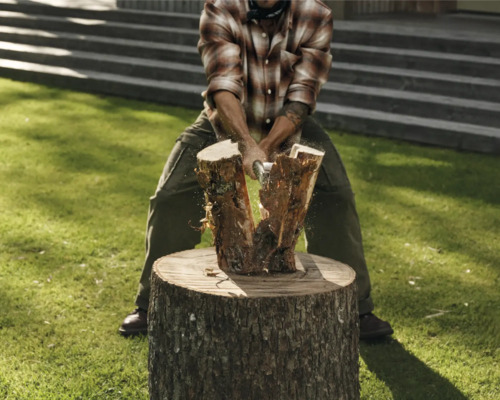 Bărbat despărțind lemne pe un butuc cu un topor.