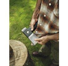 Bărbat curățând lama toporului lângă trunchiul de copac