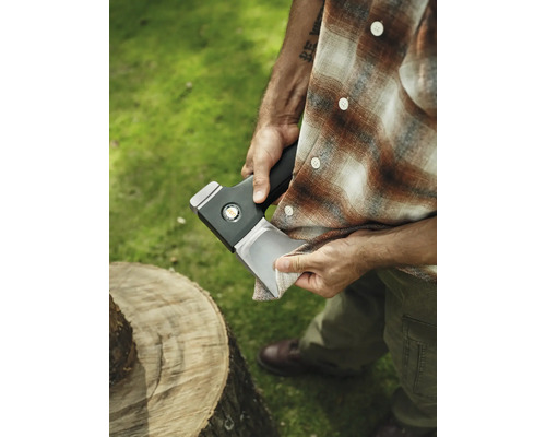 Bărbat curățând lama toporului lângă trunchiul de copac