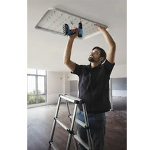 Un meseriaș instalează o lampă de plafon cu LED cu o șurubelniță fără fir într-o cameră.