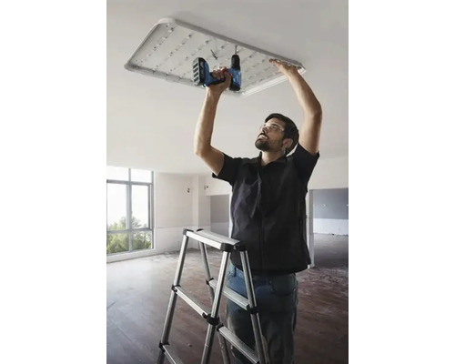 Un meseriaș instalează o lampă de plafon cu LED cu o șurubelniță fără fir într-o cameră.