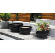 Trei jardiniere negre de diferite dimensiuni pe o treaptă de piatră cu plante