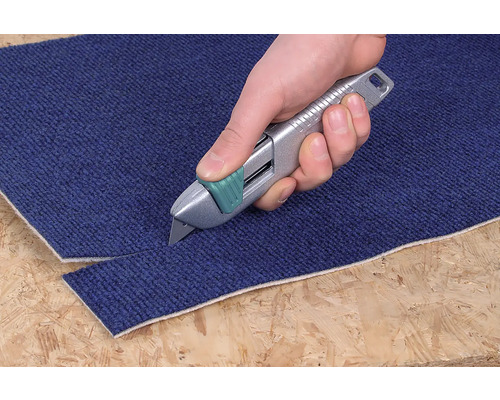 O mână taie un covor cu un cuțit de covoare.