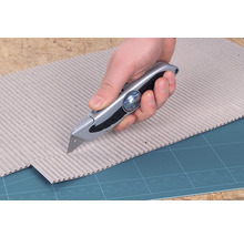 O mână taie carton cu un cuțit universal.