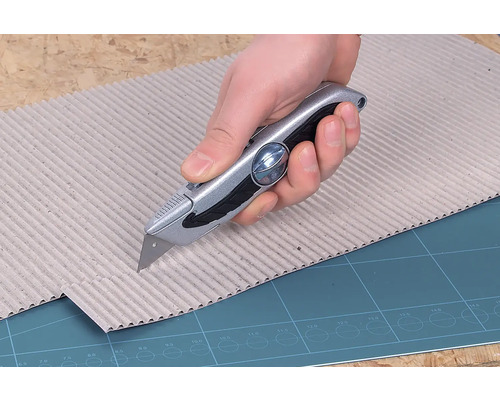 O mână taie carton cu un cuțit universal.