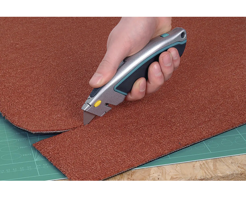 Un covor este tăiat la dimensiune cu un cuțit pentru covoare.