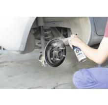 O persoană curăță o frână cu tambur deschisă a unei mașini cu curățător de frâne.