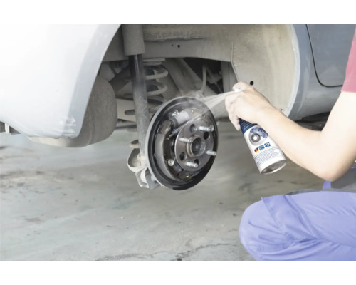 O persoană curăță o frână cu tambur deschisă a unei mașini cu curățător de frâne.