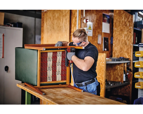 Artizan fixează tapițeria de un scaun cu un capsator