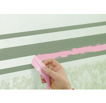 O persoană îndepărtează bandă adezivă de pe un perete cu dungi vopsite.