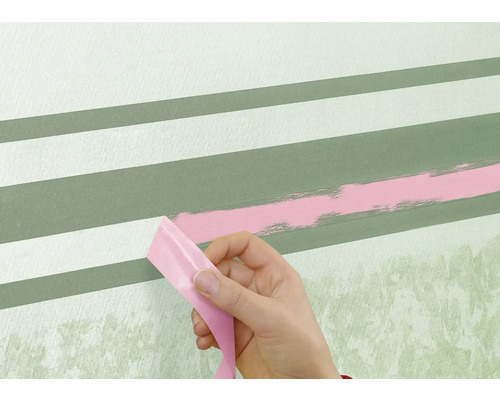 O persoană îndepărtează bandă adezivă de pe un perete cu dungi vopsite.