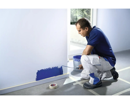 Un bărbat vopsește un perete cu o rolă de vopsea într-o cameră.