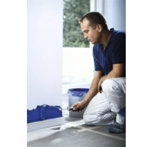 Bărbat vopsește un perete cu trafalet și vopsea dintr-o găleată