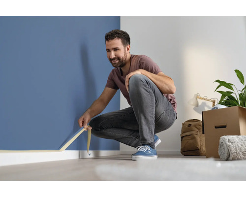 Bărbat aplicând bandă de mascare de-a lungul peretelui pentru renovare