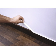 Mână fixând o plintă pe perete deasupra podelei laminate