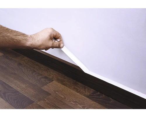 Mână fixând o plintă pe perete deasupra podelei laminate