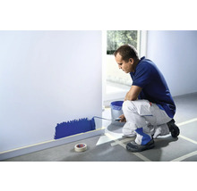 Un bărbat vopsește un perete cu trafaletul, înconjurat de bandă de mascare.