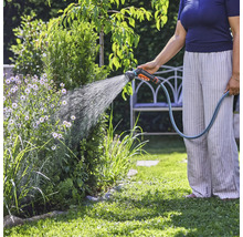 O persoană udă plantele din grădină cu un furtun de grădină.