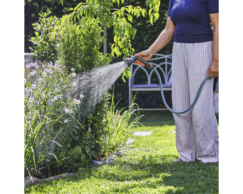 O persoană udă plantele din grădină cu un furtun de grădină.