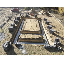 Șantier cu săpătură de fundație, izolație și blocuri de beton pregătite pentru construcția casei