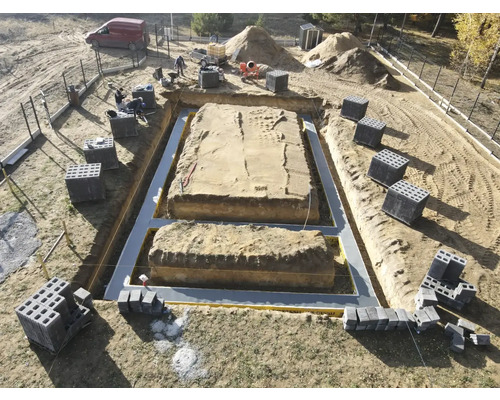 Șantier cu săpătură de fundație, izolație și blocuri de beton pregătite pentru construcția casei