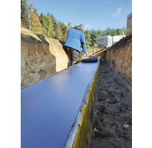 Bărbat care așterne folie de etanșare într-un șanț pentru lucrări de construcție.