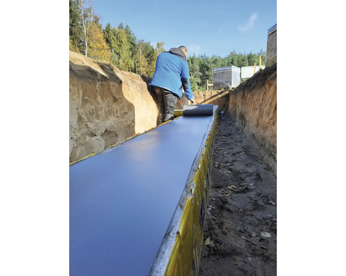 Bărbat care așterne folie de etanșare într-un șanț pentru lucrări de construcție.