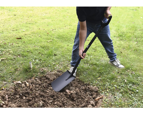 O persoană sapă în grădină cu o lopată.