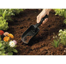 Lopată de grădină în pământ cu flori în fundal