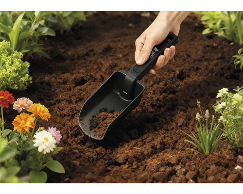 Lopată de grădină în pământ cu flori în fundal