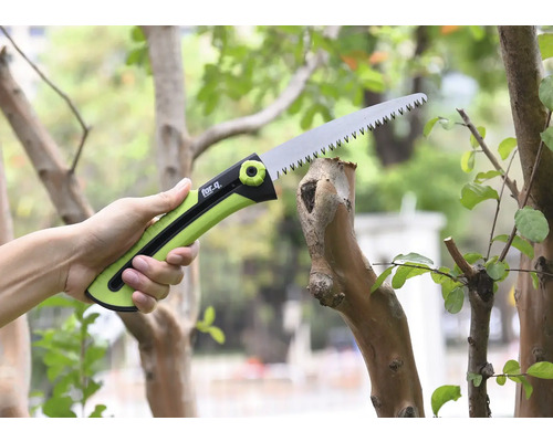 O mână ține un ferăstrău de ramuri în timp ce taie o ramură.