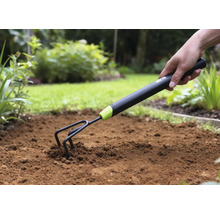 Prim-plan cu o mână care împinge o gheară de grădină în pământ