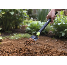 O lopată de mână cu pământ ținută pe un fundal de grădină