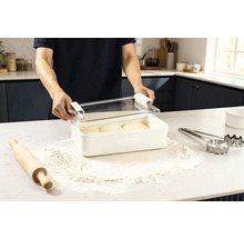 Scenă într-o bucătărie: un bărbat deschide o cutie de conservare cu aluat, înconjurat de făină, un sucitor și forme de tăiat.