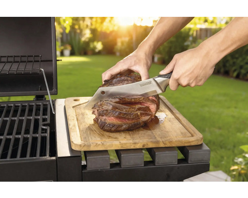 Friptura preparată este tăiată cu un cuțit pe o scândură de lemn lângă un grătar.