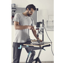 Bărbat care găurește o piesă de prelucrat cu o mașină de găurit și un suport de găurit pe un banc de lucru.