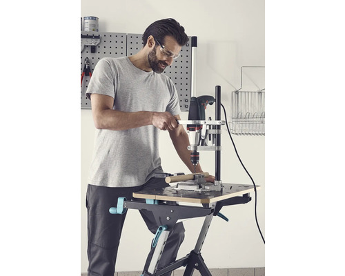 Bărbat care găurește o piesă de prelucrat cu o mașină de găurit și un suport de găurit pe un banc de lucru.