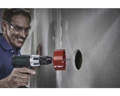 Un bărbat face o gaură într-un perete cu un ferăstrău circular.