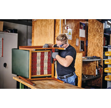 Un bărbat fixează arcul unui fotoliu cu un capsator pneumatic.