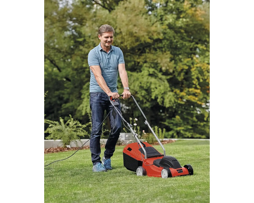 Un bărbat tunde gazonul cu o mașină de tuns iarba electrică.